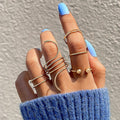 Hand wearing multiple gold rings with blue nail polish on a neutral background