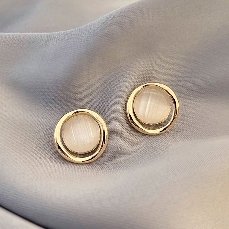 Pair of gold earrings with round, light-colored stones on a beige fabric background