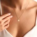 Gold necklace with a round pendant on a person wearing a white top.