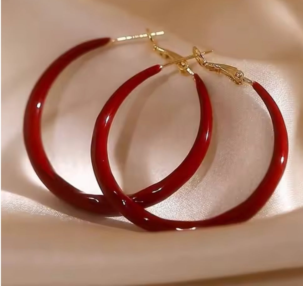 Green hoop earrings with gold clasps on a beige fabric background