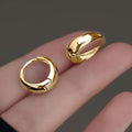 Gold hoop earrings on a hand against a dark background