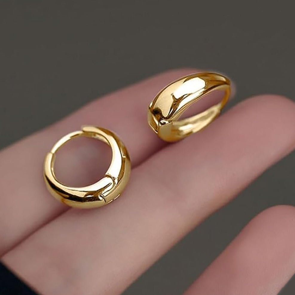 Gold hoop earrings on a hand against a dark background