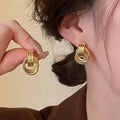 Gold hoop earrings being worn and held up to the ear against a neutral background