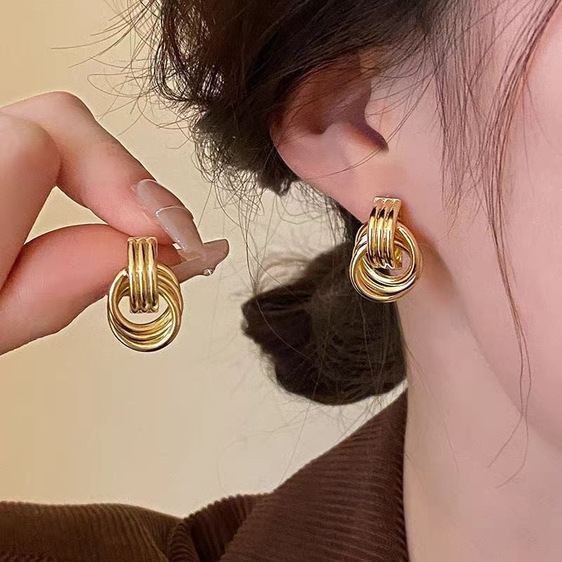 Gold hoop earrings being worn and held up to the ear against a neutral background