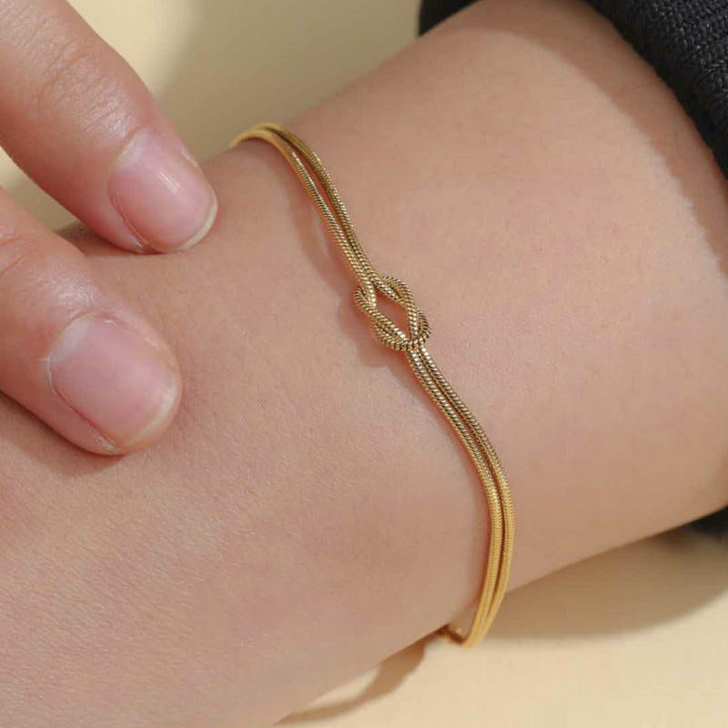 Gold bracelet with a knot design on a wrist against a light background