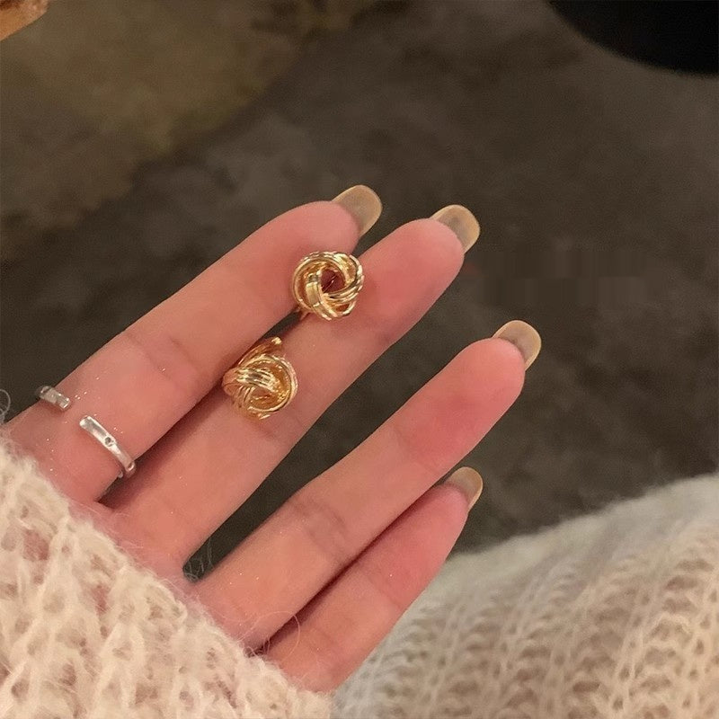 Gold earrings held in a hand with a blurred background