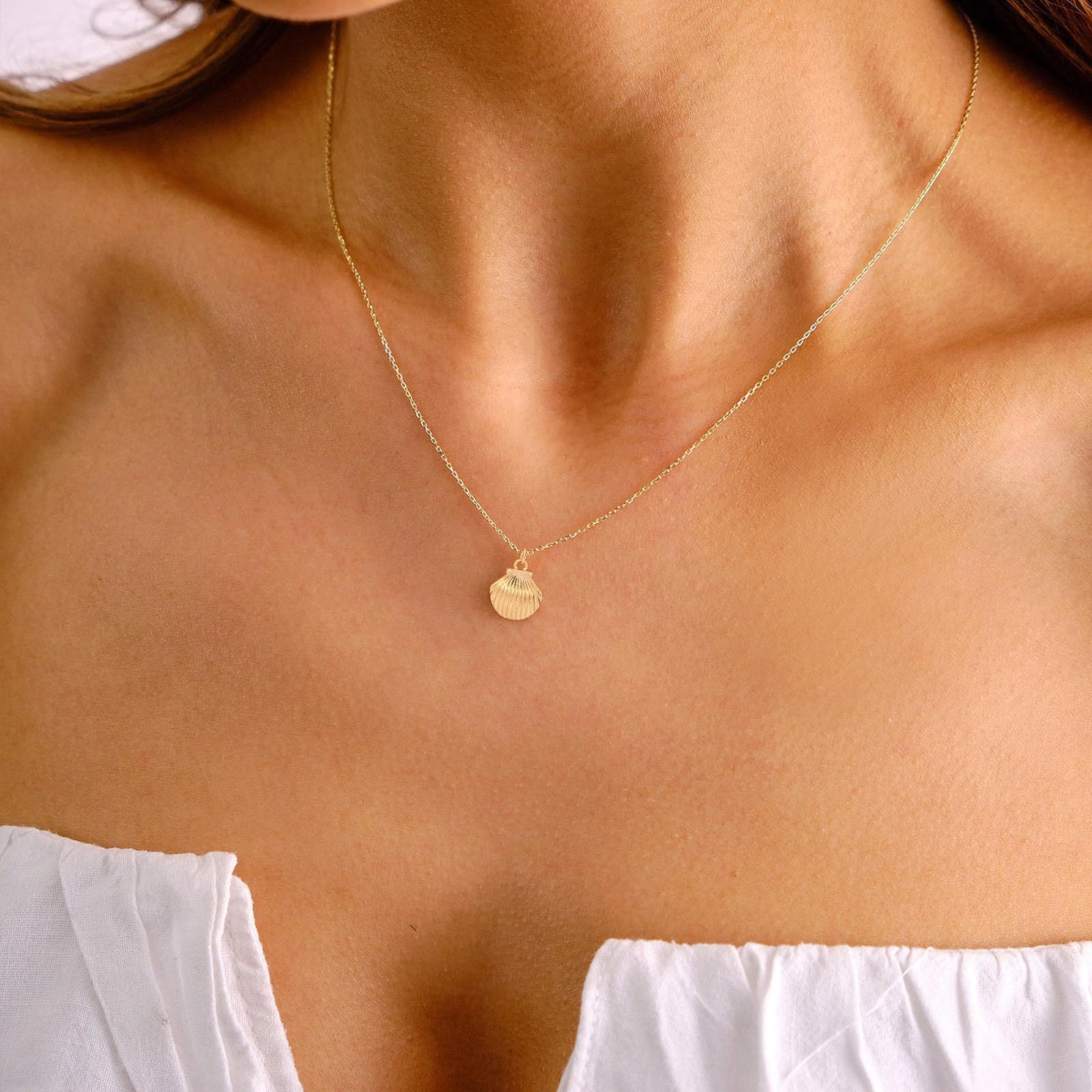 Gold necklace with a heart pendant on a person wearing a white top.