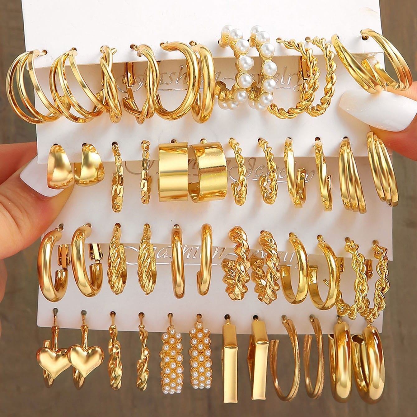 Assorted gold hoop earrings on a display card held by a hand.