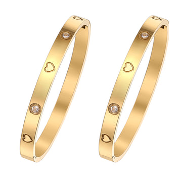Two gold bangles with heart and diamond designs on a white background