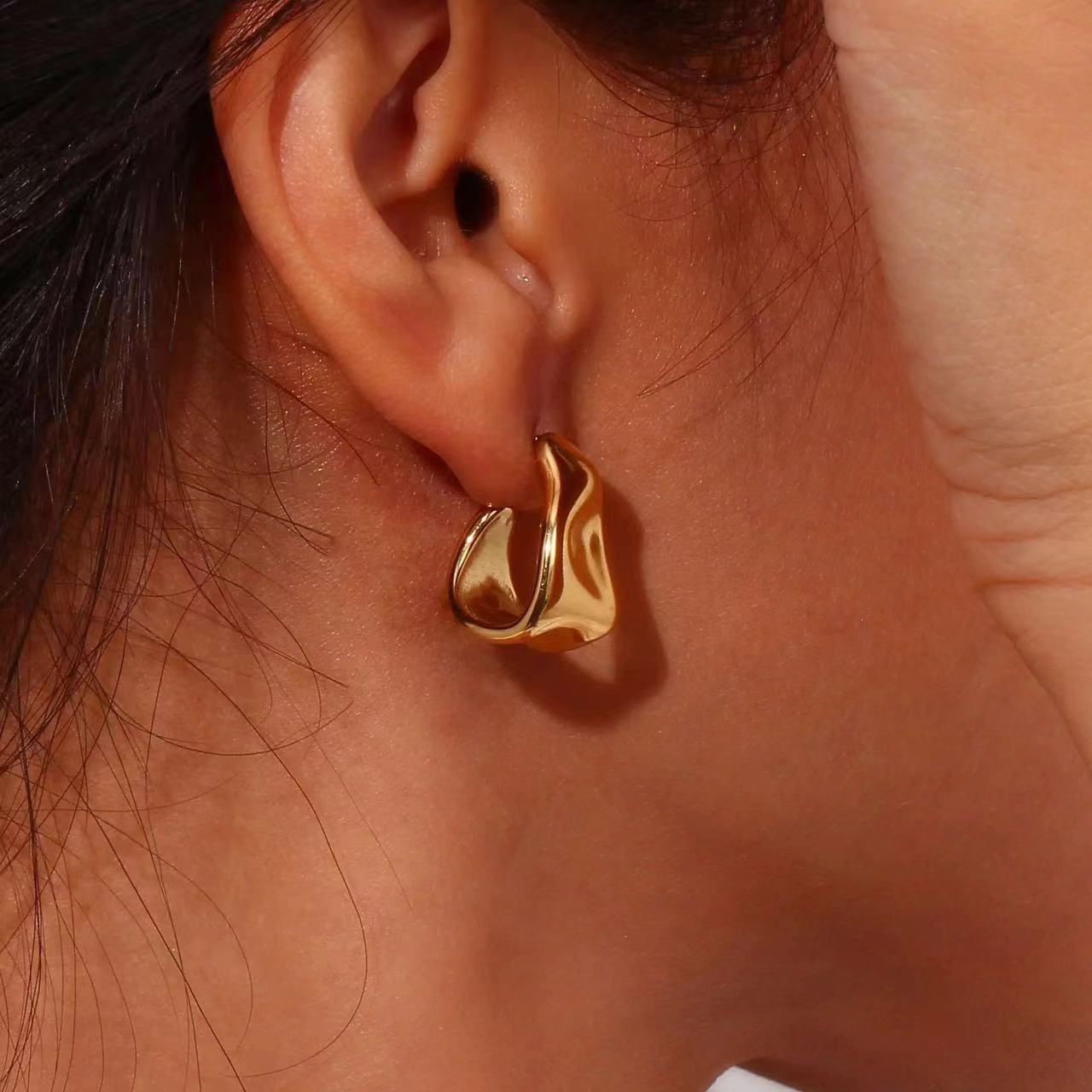 Gold hoop earring worn by a person with a neutral background