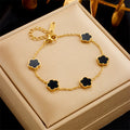 Gold bracelet with black clover-shaped charms on a beige jewelry box
