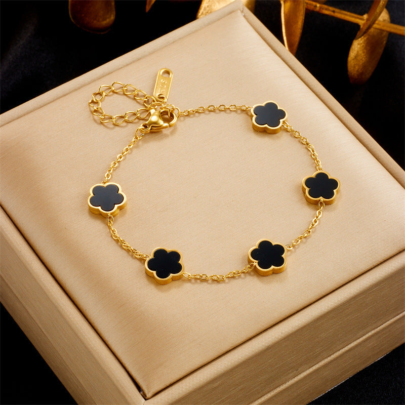 Gold bracelet with black clover-shaped charms on a beige jewelry box