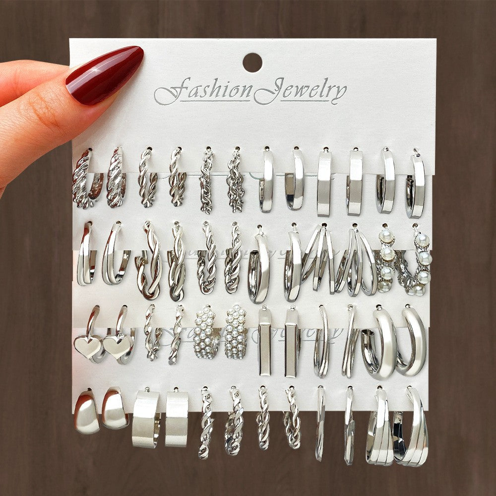 Hand holding a card with various silver earrings on a brown background