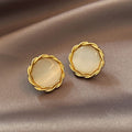 Pair of gold earrings with round, light-colored stones on a beige fabric background