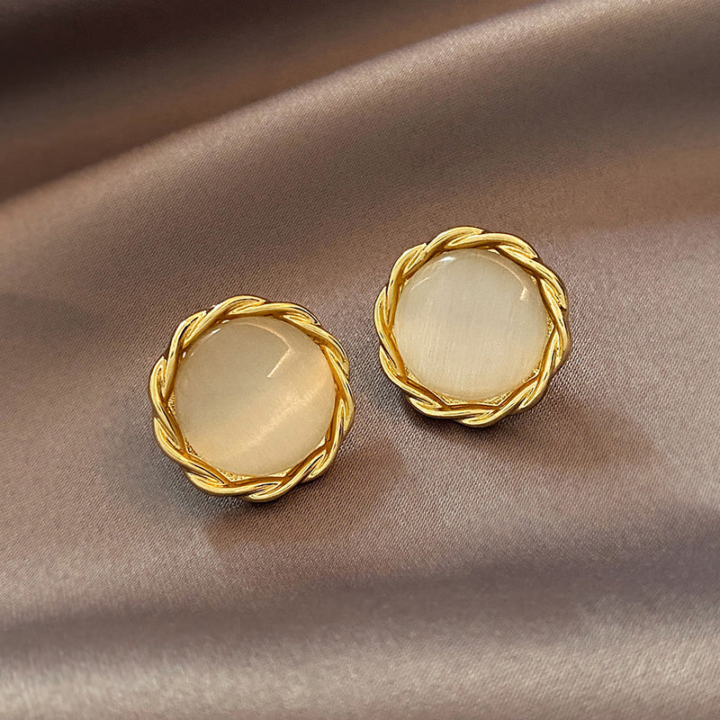 Pair of gold earrings with round, light-colored stones on a beige fabric background