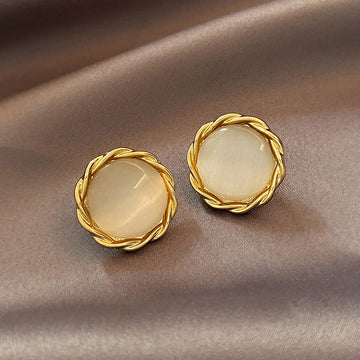 Pair of gold earrings with round, light-colored stones on a beige fabric background