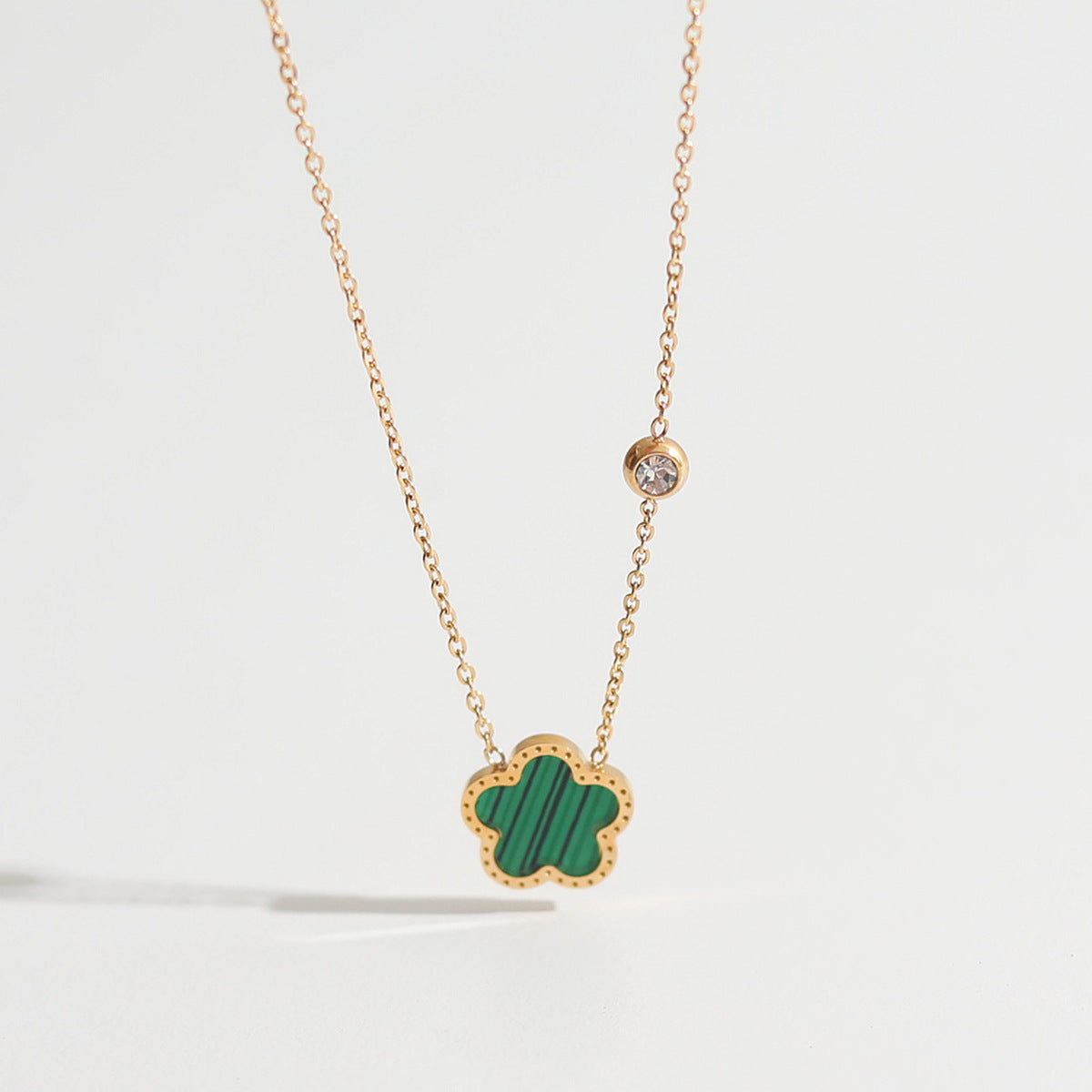 Gold necklace with a green clover pendant on a light gray background