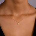 Gold necklace with a pendant on a person's neck against a neutral background