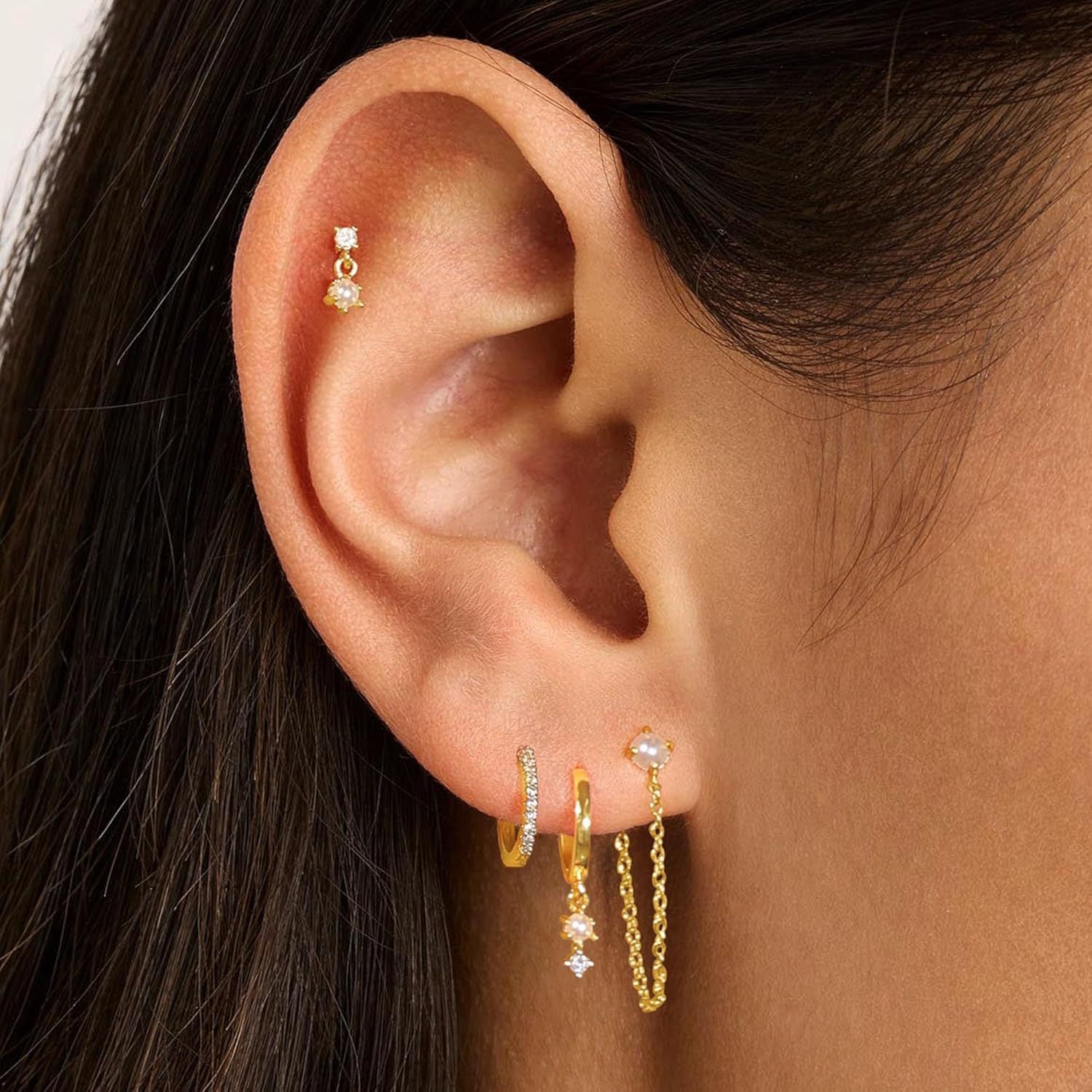 Close-up of an ear wearing gold hoop earrings with small gemstones.