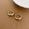 Gold hoop earrings on a beige surface with a white dish in the background