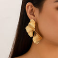 Gold leaf-shaped earring worn by a person with a neutral background