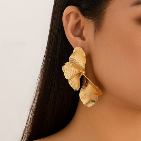 Gold leaf-shaped earring worn by a person with a neutral background
