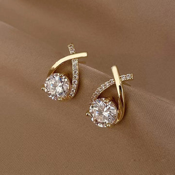 Gold earrings with clear gemstones on a beige fabric background