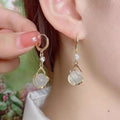 Close-up of a person wearing gold earrings with clear stones.