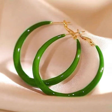 Green hoop earrings with gold clasps on a beige fabric background
