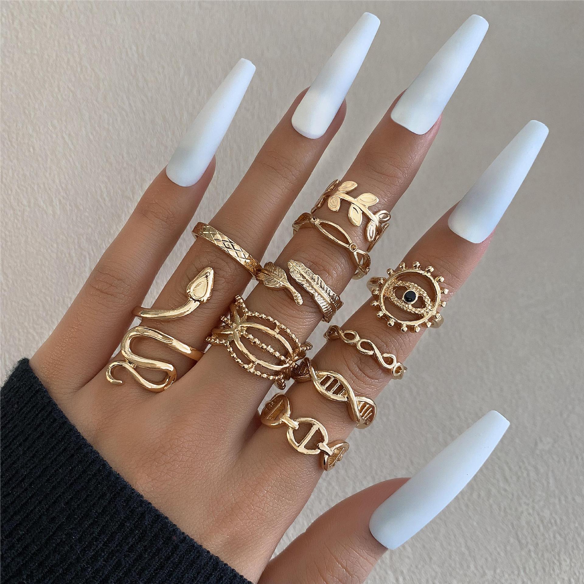 Hand wearing multiple gold rings with white nail polish on a neutral background