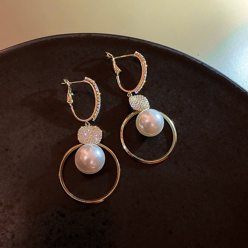 Pair of gold hoop earrings with pearl-like beads on a dark surface