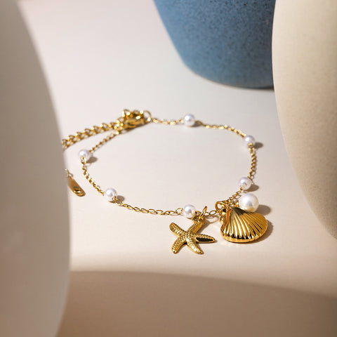 Gold bracelet with starfish and shell charms on a neutral background