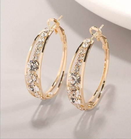 Gold hoop earrings with clear gemstones on a light gray background
