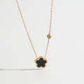 Gold necklace with a black clover pendant on a white background