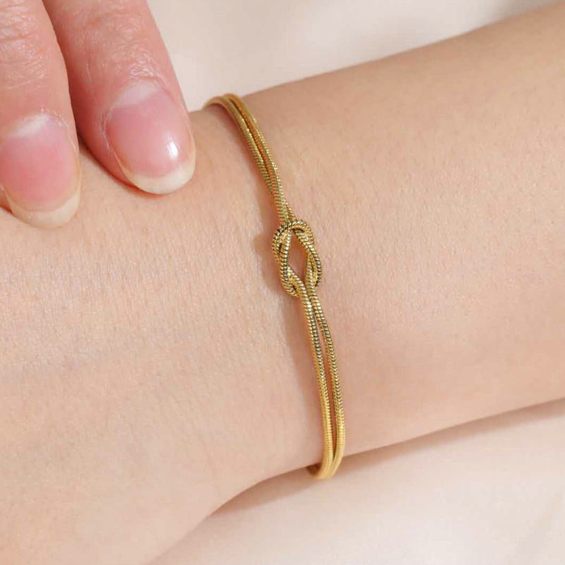 Gold bracelet with a knot design on a wrist against a light background