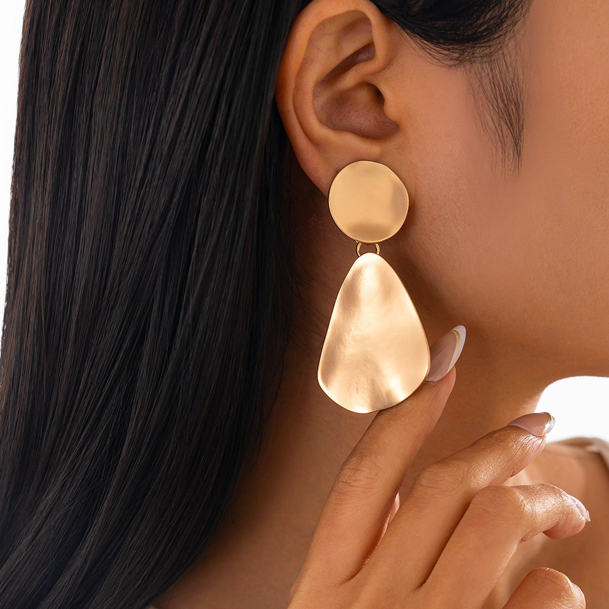 Gold earrings worn by a person with dark hair and a neutral background